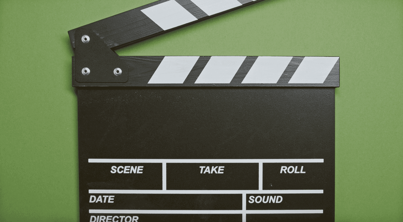 A black film clapperboard open on a green background