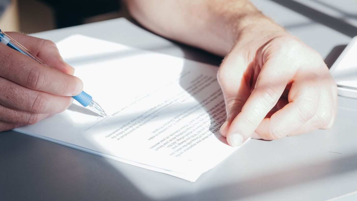 Hands signing a printed document with a blue pen